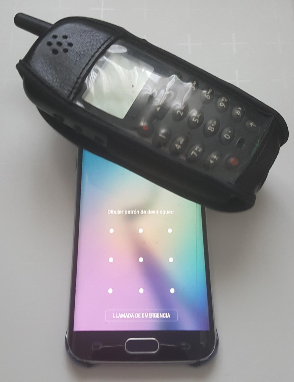 Móvil antiguo con teclado numérico sobre un móvil más moderno de pantalla táctil mostrando el patrón de desbloqueo
